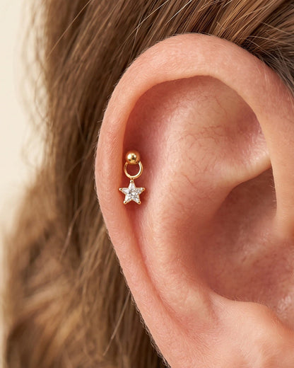 Close-up of an ear with gold and star-shaped earrings on a neutral background